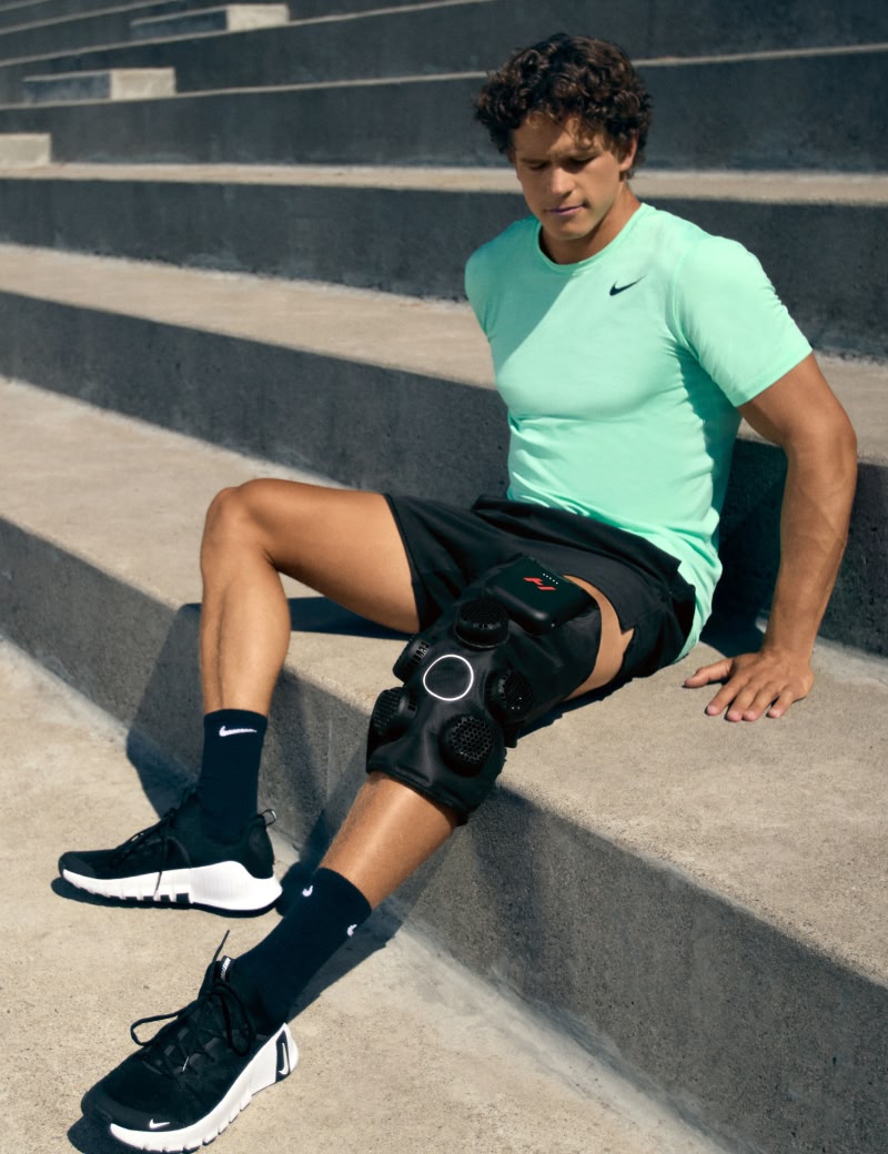 Man sitting on steps wearing a green Nike shirt hyperice x 2 knee device.